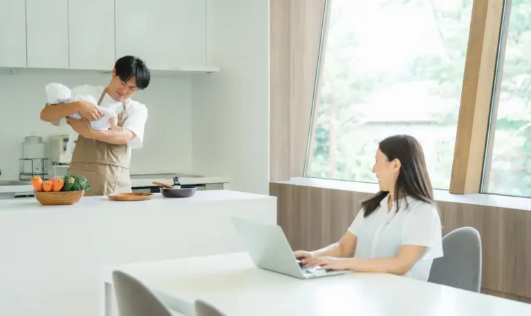 キッチンで育児をする夫とダイニングテーブルで仕事をする妻