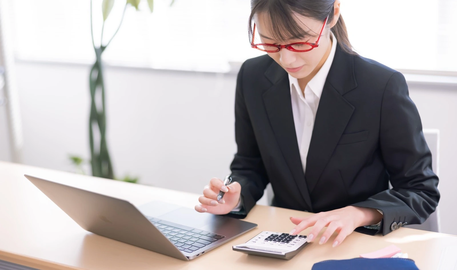 電卓とノートPCで給与計算をする人事担当者