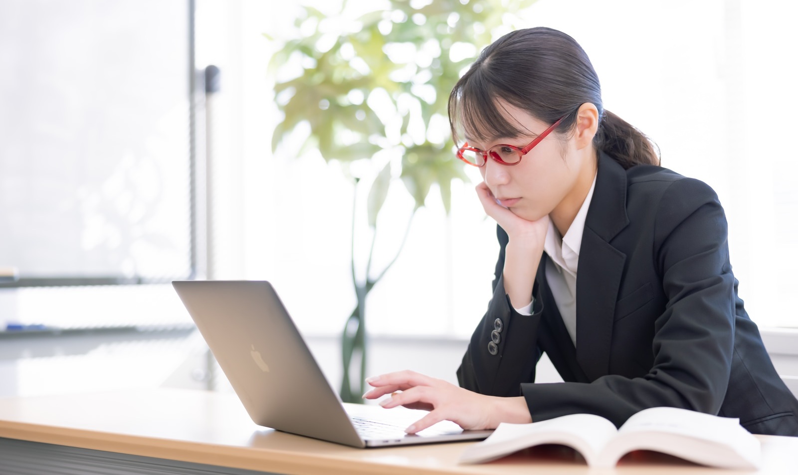 頬杖をついてPCの画面を眺める眼鏡をかけた女性社員