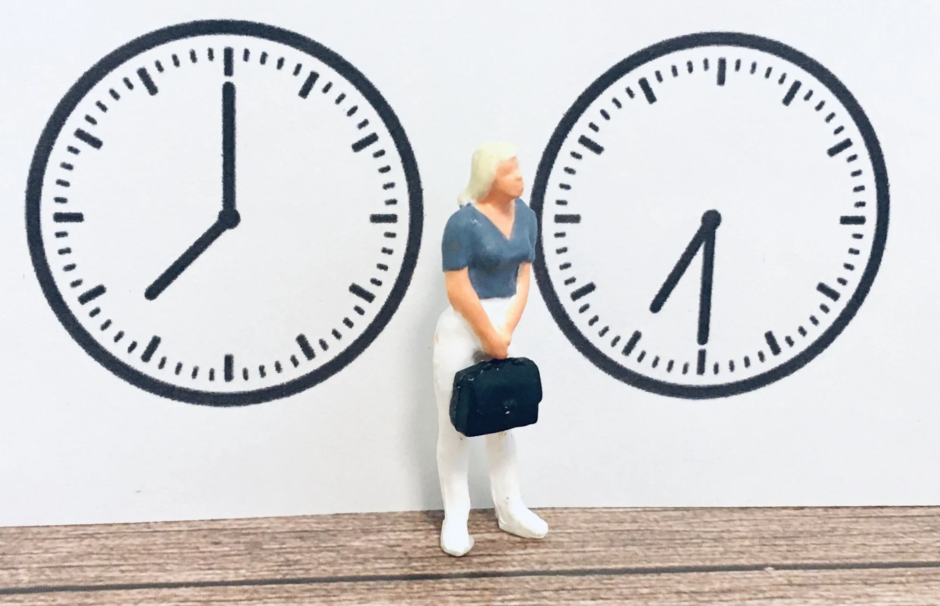 ２つの時計のイラストとその間にカバンを持った女性の人形