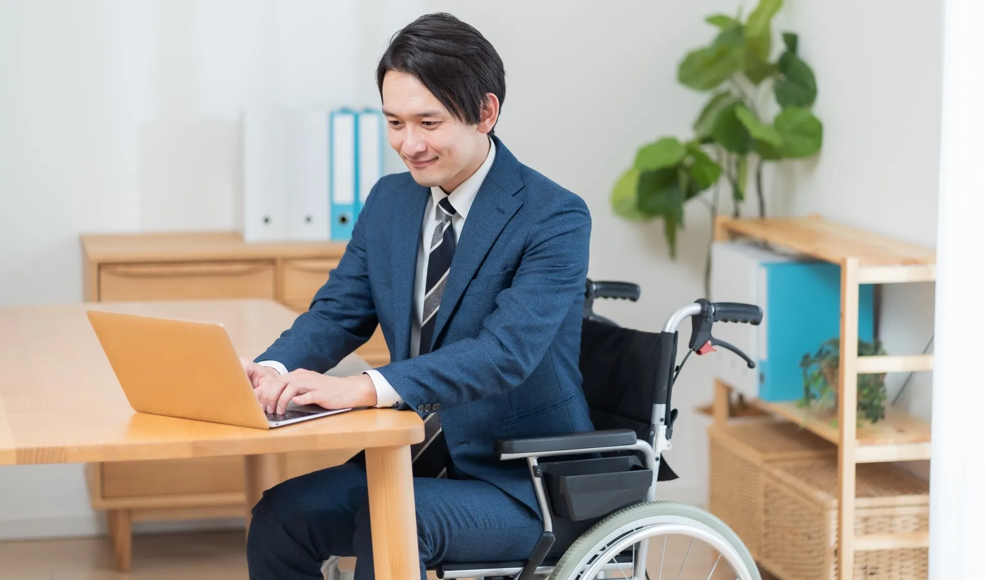車いすに乗った男性者員が机の上でPCを操作している